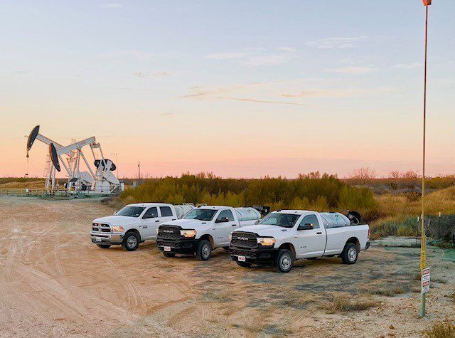 Three white trucks parked in front of an oil pump, showcasing a scene of industrial activity