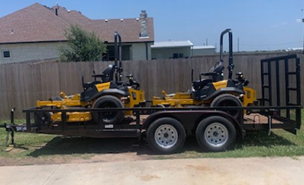 Two yellow mowers on the trailer parked on the green lush field